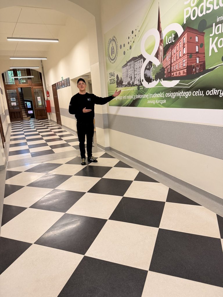 Pracownik wallKing prezentuje mural na 80-lecie szkoły z cytatem Janusza Korczaka na ścianie korytarza