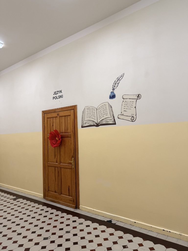 Napis JĘZYK POLSKI z ilustracją otwartej księgi, pióra i zwoju pergaminu nad drzwiami sali
