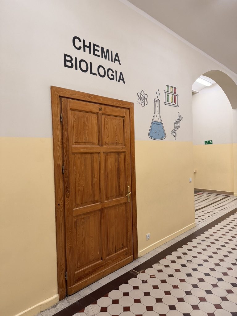 Napis CHEMIA BIOLOGIA z ilustracjami kolby, probówek, atomu i helisy DNA nad drzwiami sali