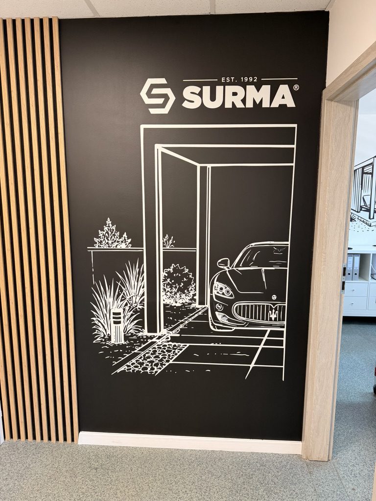 Czarna ściana z logo SURMA i kreskową grafiką pergoli z samochodem, druk wielkoformatowy w biurze