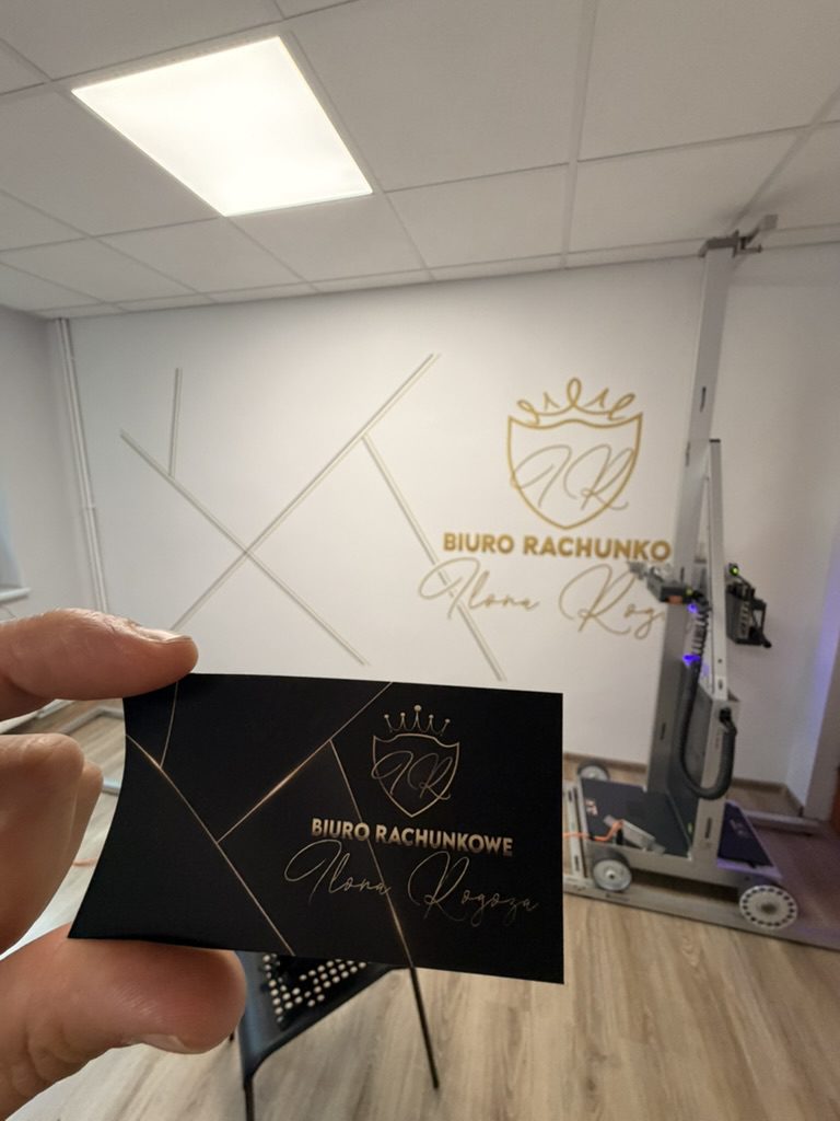 Wizytówka Biura Rachunkowego Ilona Rogoza na tle złotego logo wydrukowanego na ścianie – spójna identyfikacja wizualna