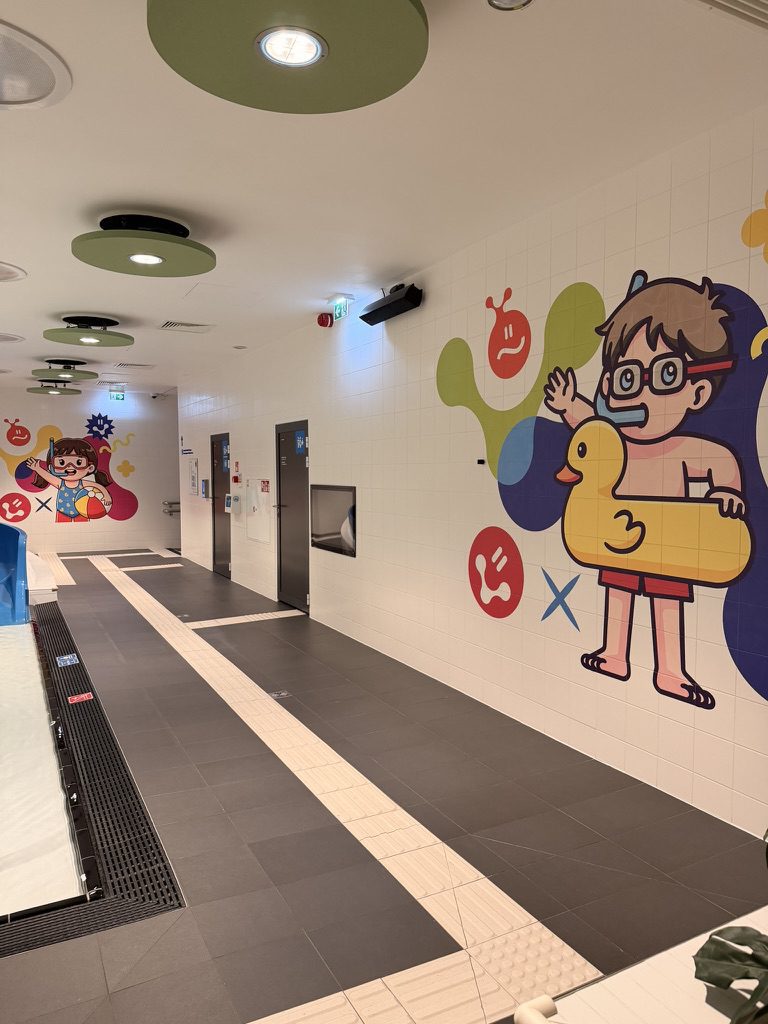 Korytarz przy basenie dla dzieci z dwoma kolorowymi muralami wydrukowanymi na kafelkach