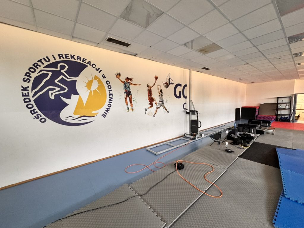 Logo Ośrodka Sportu i Rekreacji w Goleniowie i sylwetki sportowców wydrukowane na ścianie sali