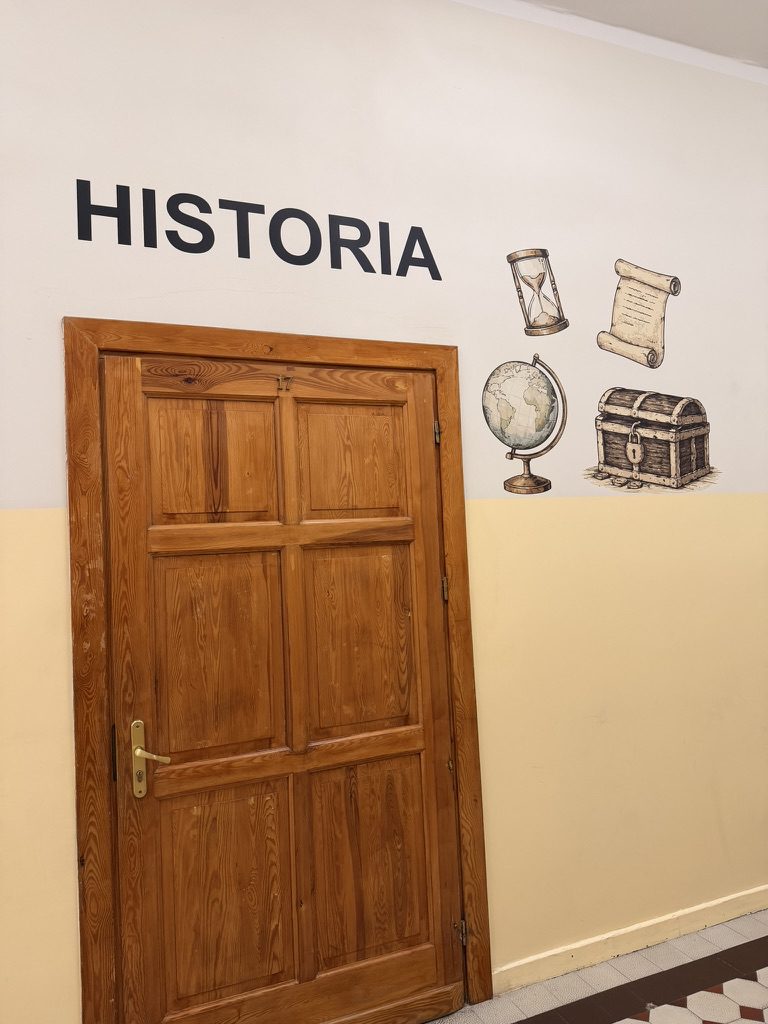 Napis HISTORIA z ilustracjami klepsydry, zwoju, globusa i skrzyni ze skarbami nad drzwiami sali