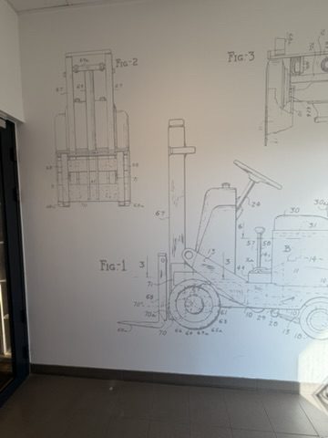 Rysunki techniczne FIG. 1, FIG. 2 i FIG. 3 wózka widłowego na ścianie recepcji zakładu KION Group